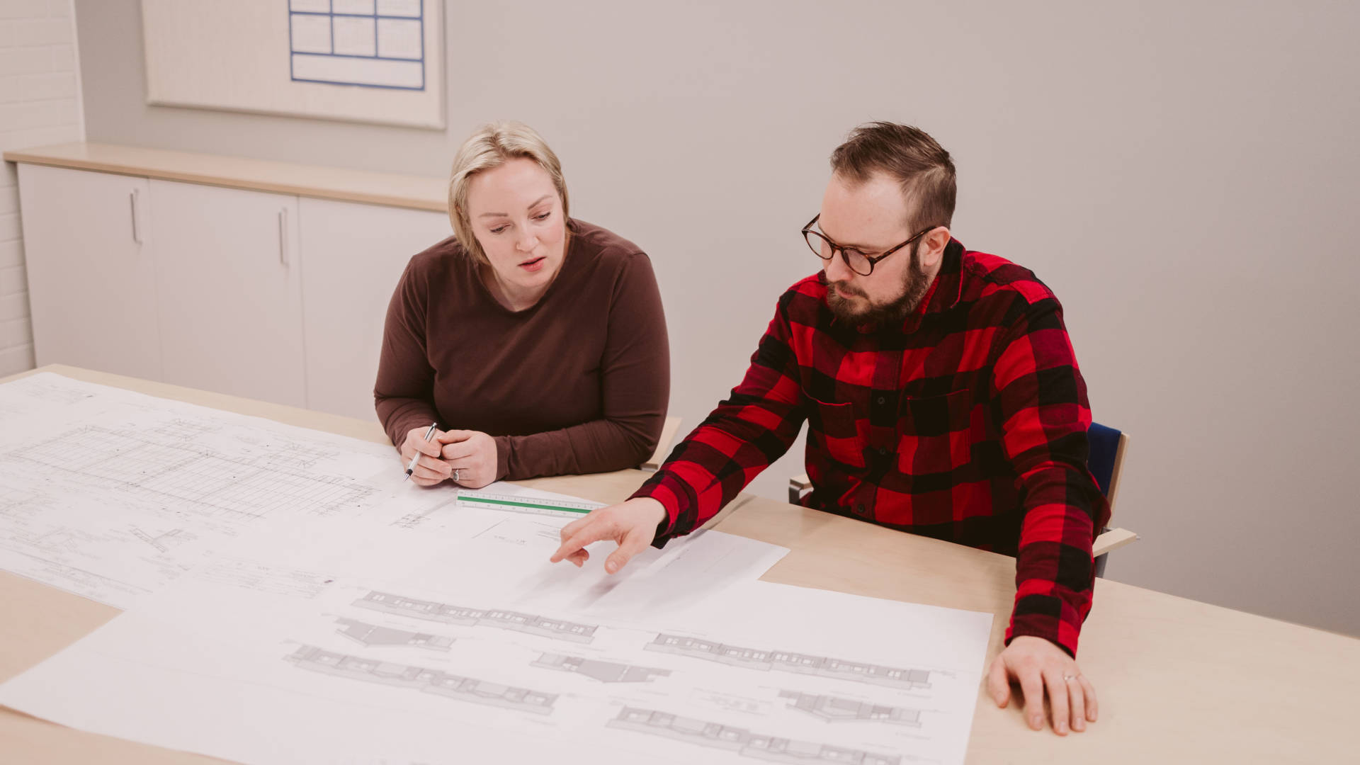 Kaksi teknisen suunnittelun opiskelijaa tutkivat yhdessä rakennuksen piirustuksia yhdessä pöydän ääressä.